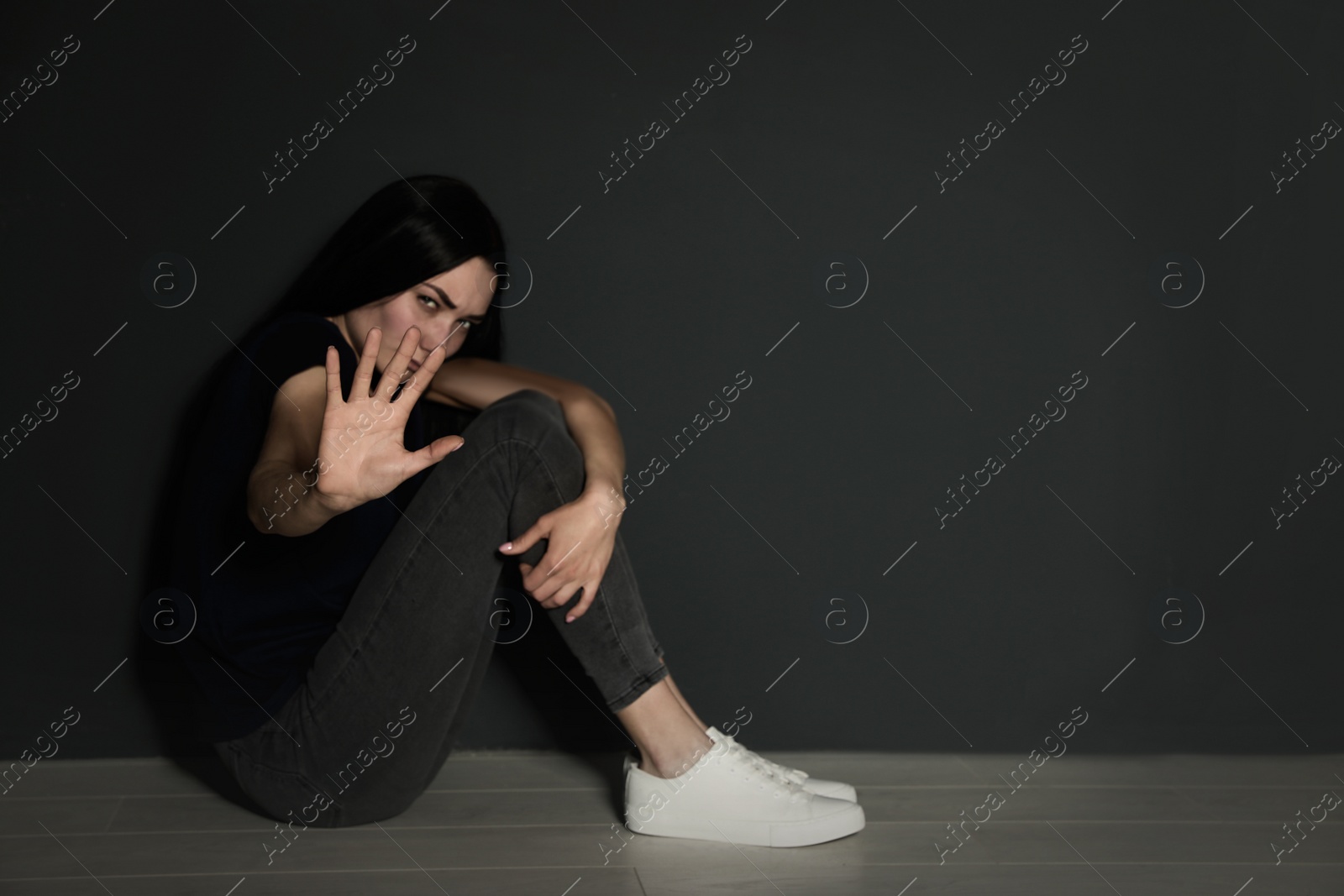 Photo of Young woman making stop gesture while sitting on floor near grey wall. Space for text