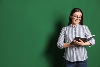 Portrait of young teacher with book on green background. Space for text