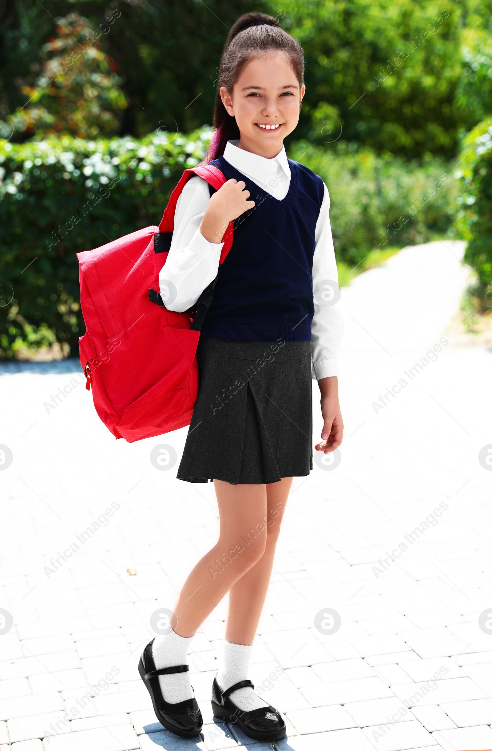 Photo of Cute little girl in school uniform with red backpack on street