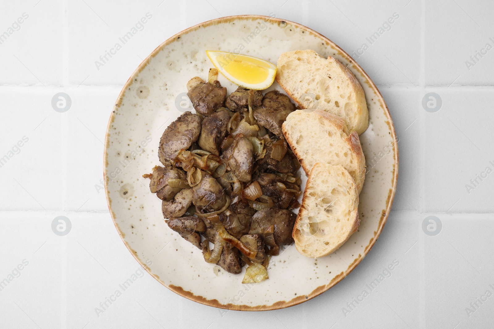 Photo of Tasty fried chicken liver served with lemon and bread on white tiled table, top view