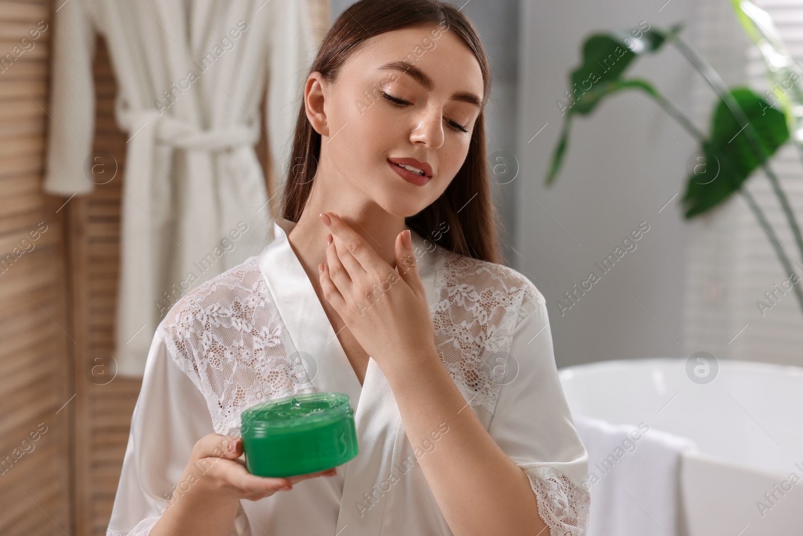 Photo of Young woman applying aloe gel onto her neck in bathroom