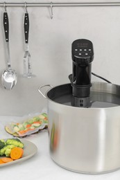 Photo of Sous vide cooker in pot and ingredients on white table. Thermal immersion circulator
