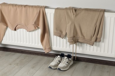 Photo of Heating radiator with sweatshirt, pants and sneakers indoors
