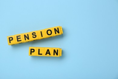 Yellow cubes with phrase Pension Plan on light blue background, flat lay. Space for text
