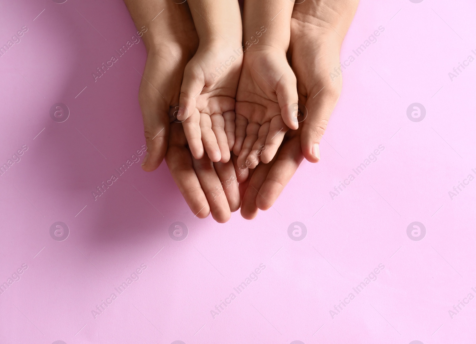 Photo of Mother holding hands with her child on pink background, top view. Happy family