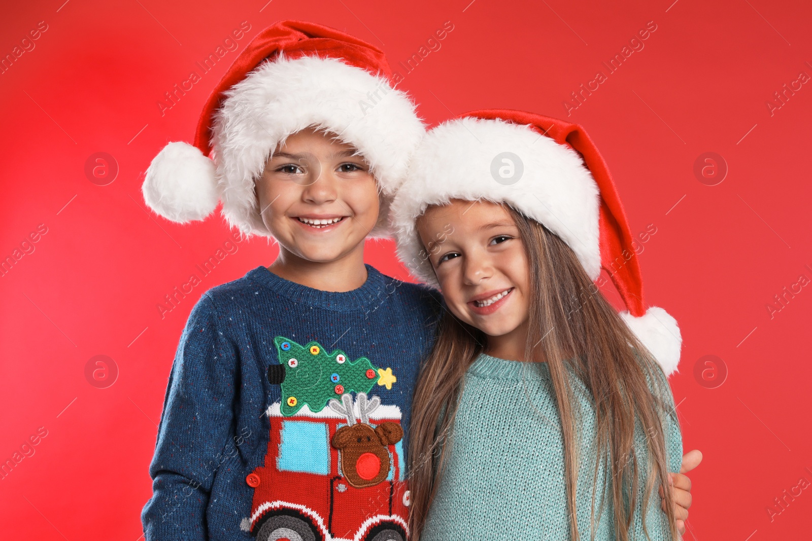 Photo of Happy little children in Santa hats on red background. Christmas celebration