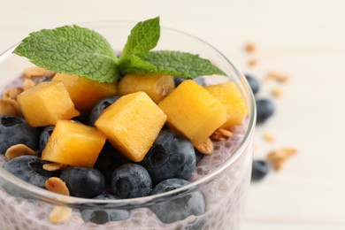 Photo of Delicious chia pudding with blueberries, mango and mint in glass on white table, closeup