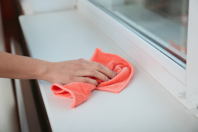 Photo of Woman cleaning window sill with cloth, closeup