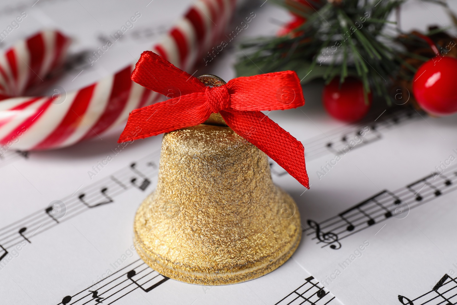 Photo of Golden shiny bell with red bow and Christmas decor on music sheets, closeup
