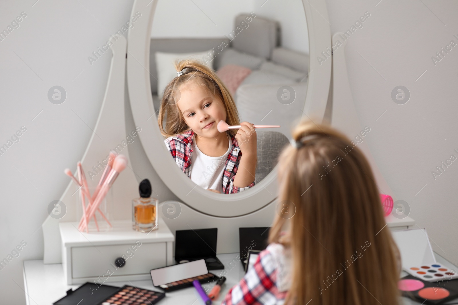 Photo of Adorable little girl applying makeup at dressing table indoors