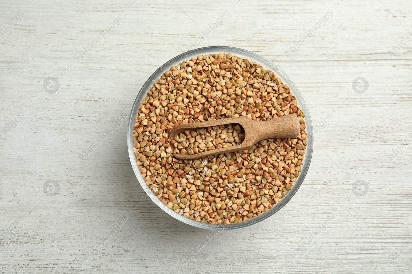 Photo of Uncooked green buckwheat grains in bowl on white wooden table, top view