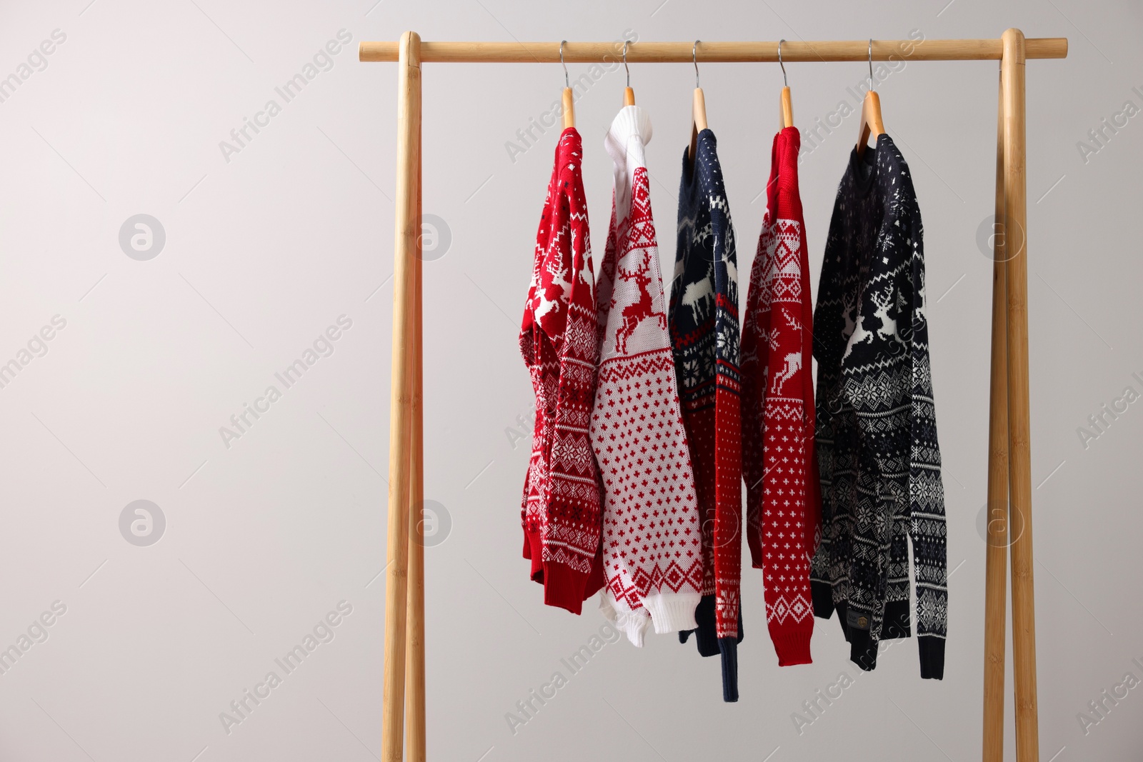 Photo of Rack with different Christmas sweaters on light background, space for text