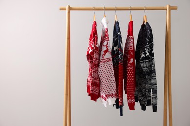 Photo of Rack with different Christmas sweaters on light background, space for text