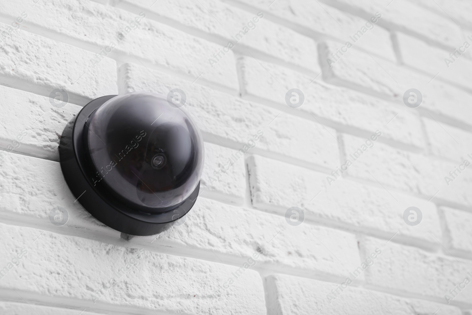 Photo of Modern CCTV security camera on white brick wall. Space for text