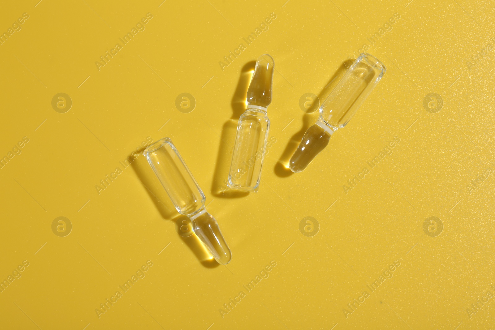 Photo of Glass ampoules with liquid on yellow background, flat lay