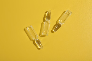 Glass ampoules with liquid on yellow background, flat lay