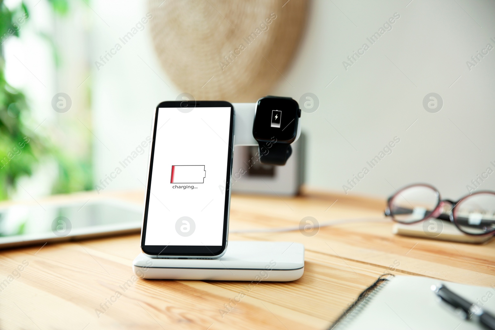 Photo of Mobile phone and smartwatch with wireless charger on wooden table. Modern workplace accessory