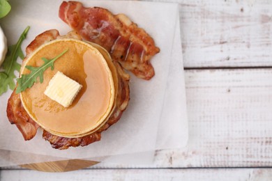 Photo of Delicious pancakes with bacon, butter, arugula and honey on table, top view. Space for text