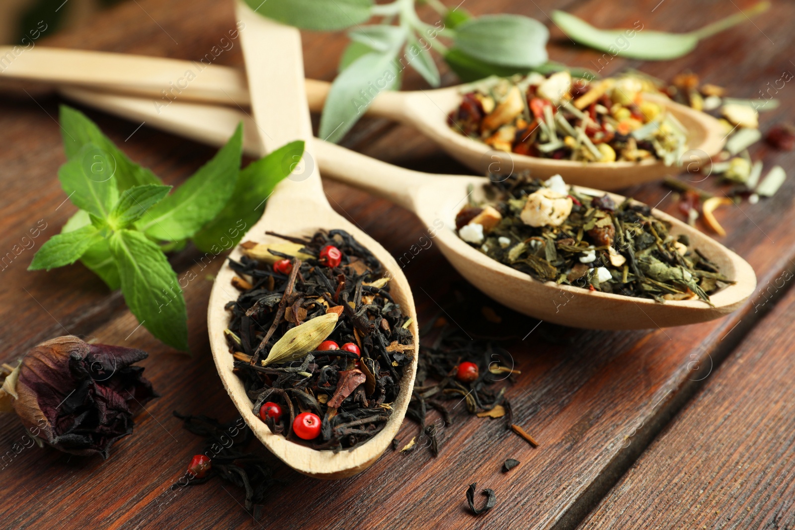 Photo of Spoons with dried herbal tea leaves on wooden table, closeup