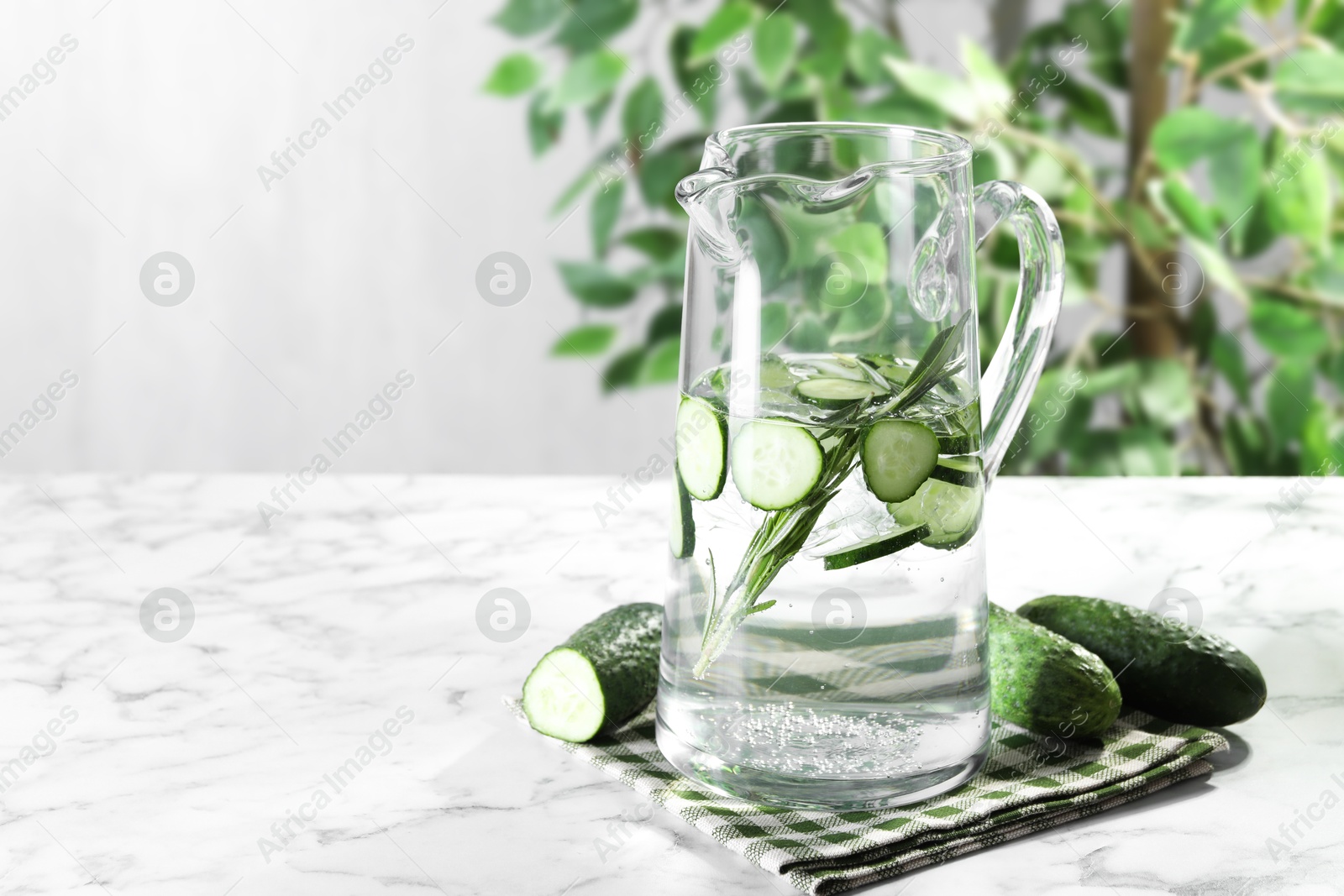 Photo of Refreshing cucumber water with rosemary in jug and vegetables on white marble table. Space for text