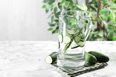 Photo of Refreshing cucumber water with rosemary in jug and vegetables on white marble table. Space for text