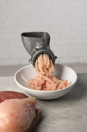 Metal meat grinder with mince, raw chicken and beef on grey table near light wall