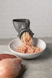 Photo of Metal meat grinder with mince, raw chicken and beef on grey table near light wall