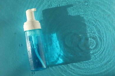 Photo of Bottle of cosmetic product in water on turquoise background, top view. Space for text