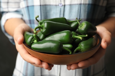 Photo of Young woman holding wooden bowl with green hot chili peppers, closeup