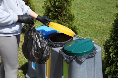 Woman throwing trash bag full of garbage in bin outdoors, closeup. Recycling concept