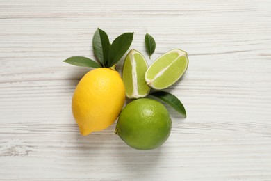 Photo of Fresh ripe lemon, limes and green leaves on white wooden background, flat lay