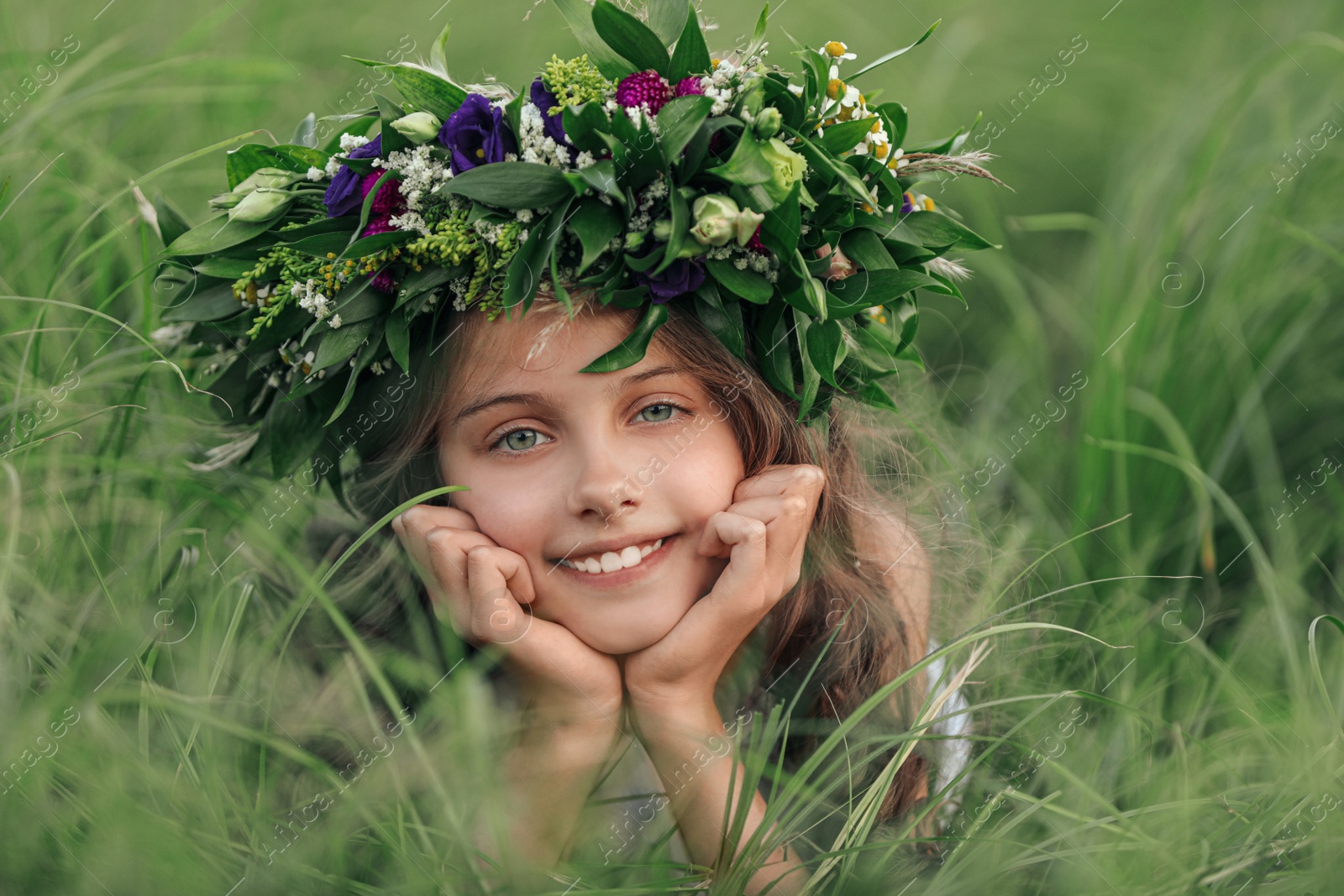 Photo of Cute little girl wearing wreath made of beautiful flowers in field