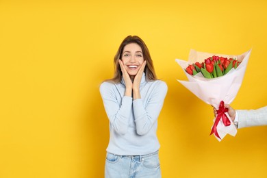 Photo of Happy woman receiving red tulip bouquet from man on yellow background. 8th of March celebration
