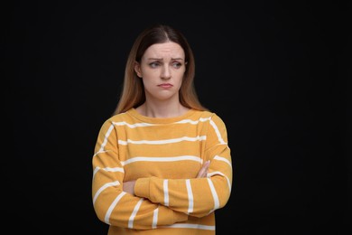 Portrait of sad woman with crossed arms on black background
