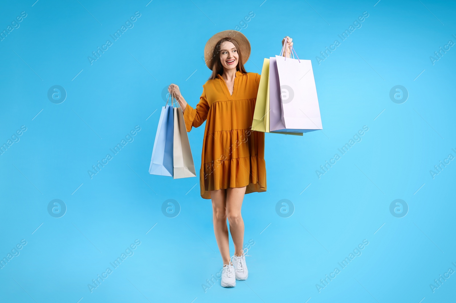 Photo of Beautiful young woman with paper shopping bags on light blue background