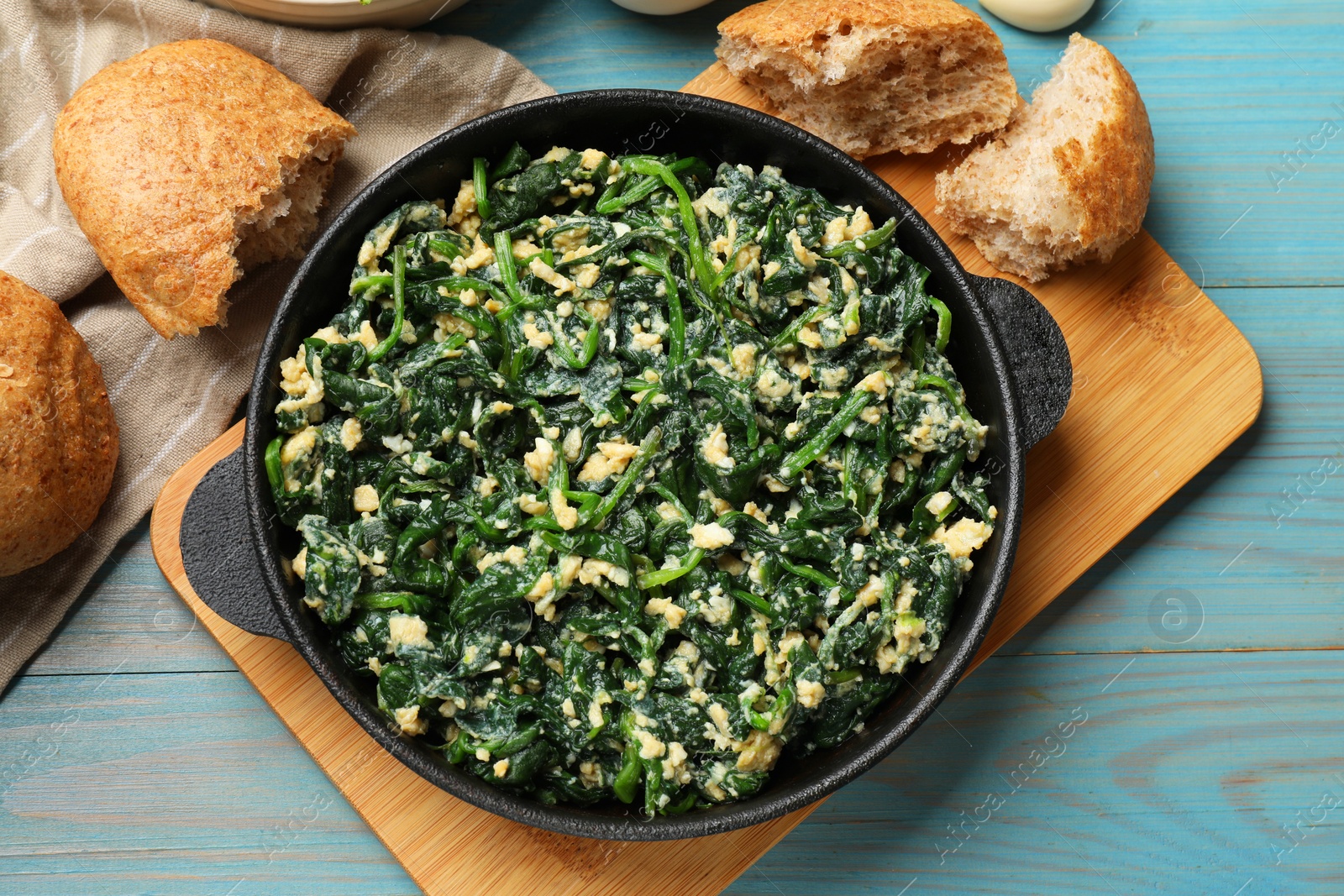 Photo of Tasty spinach dip with eggs in dish served on light blue wooden table, flat lay