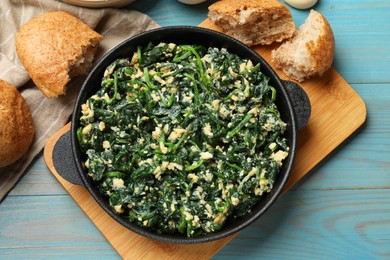 Photo of Tasty spinach dip with eggs in dish served on light blue wooden table, flat lay