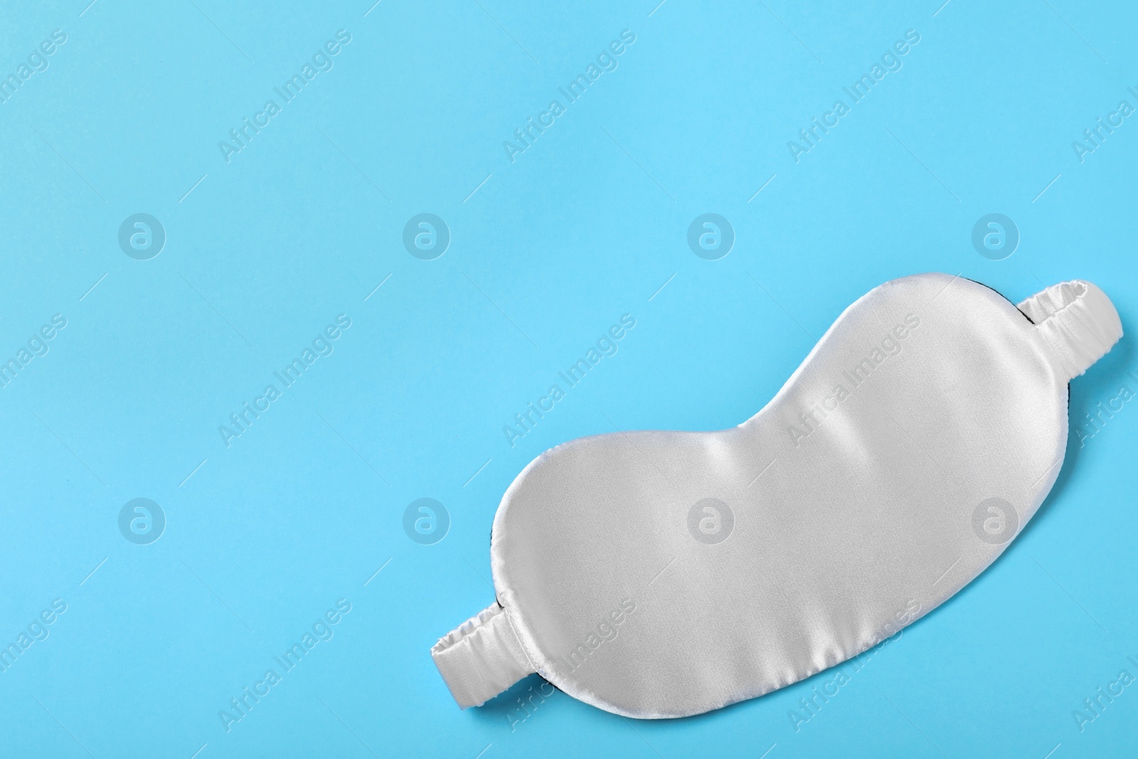 Photo of White sleeping mask on light blue background, top view with space for text. Bedtime accessory