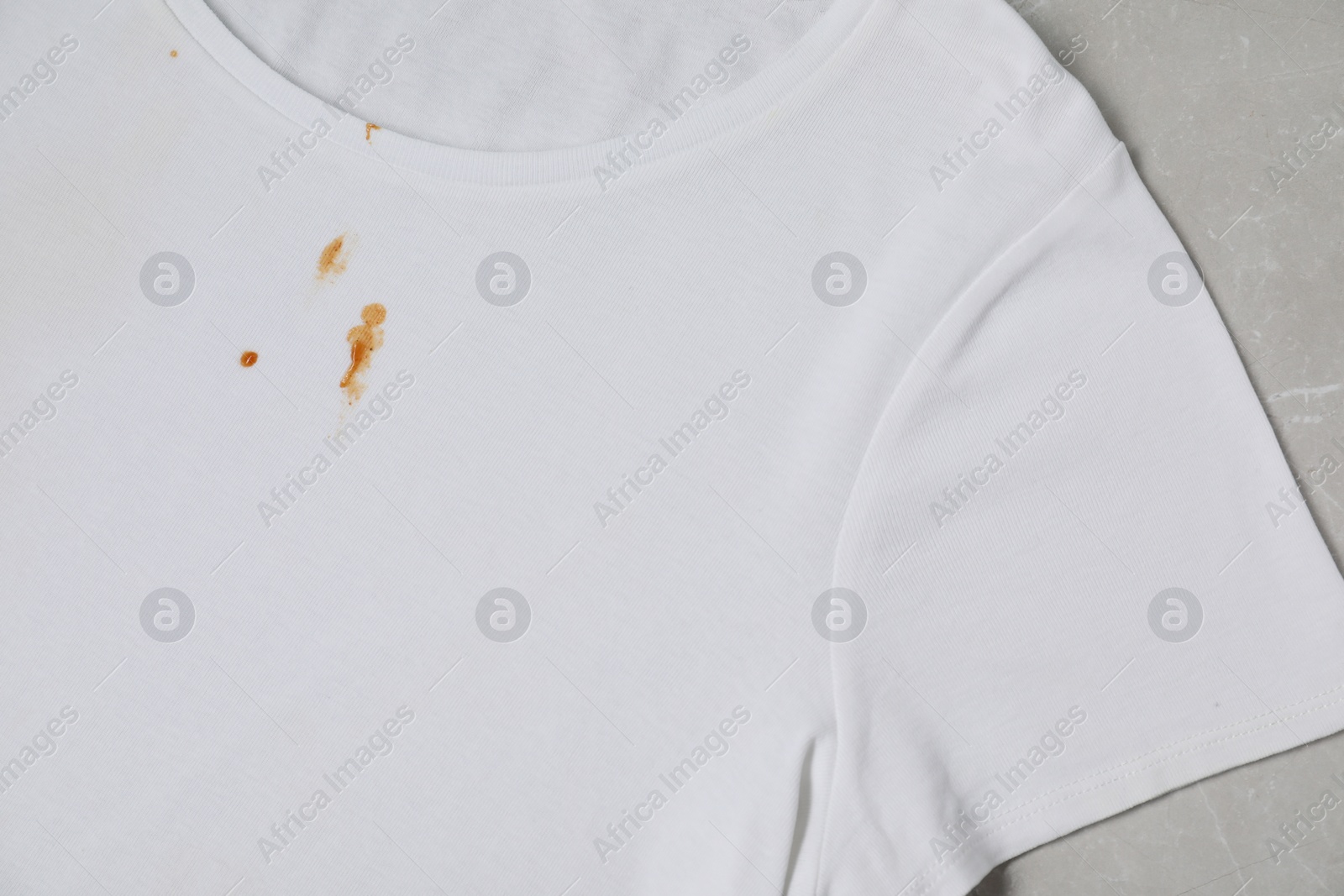 Photo of Dirty t-shirt with stains of sauce on light grey marble table, top view