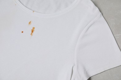 Dirty t-shirt with stains of sauce on light grey marble table, top view