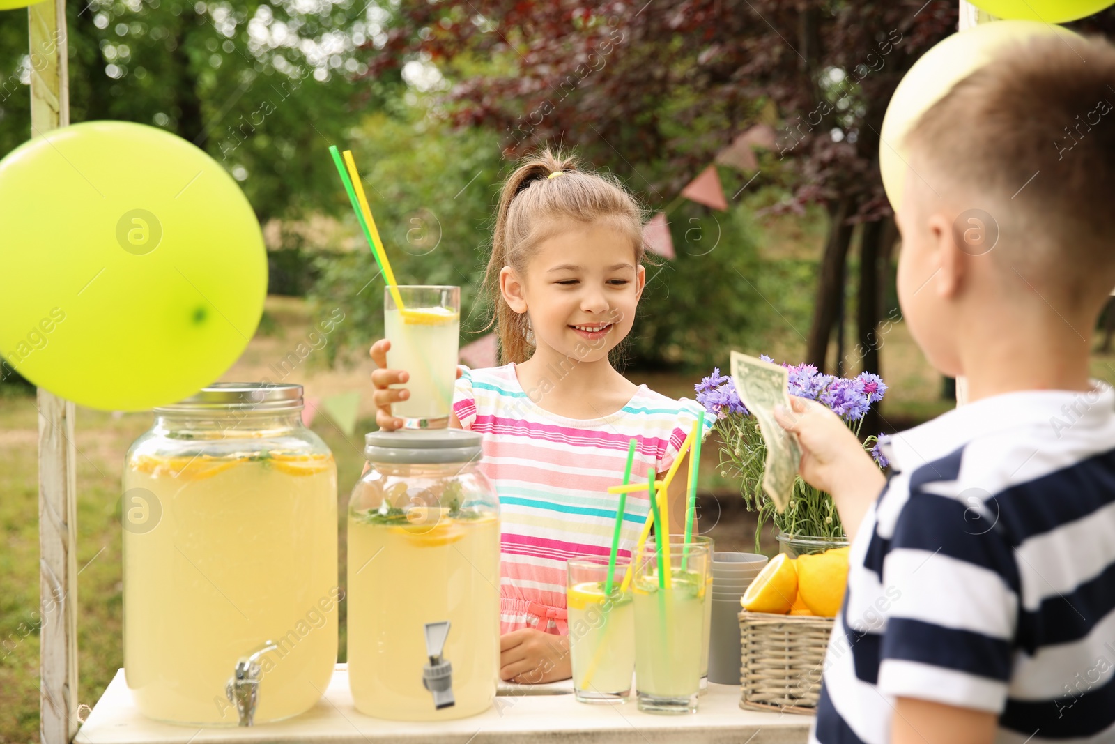 Photo of Little girl selling natural lemonade at stand in park