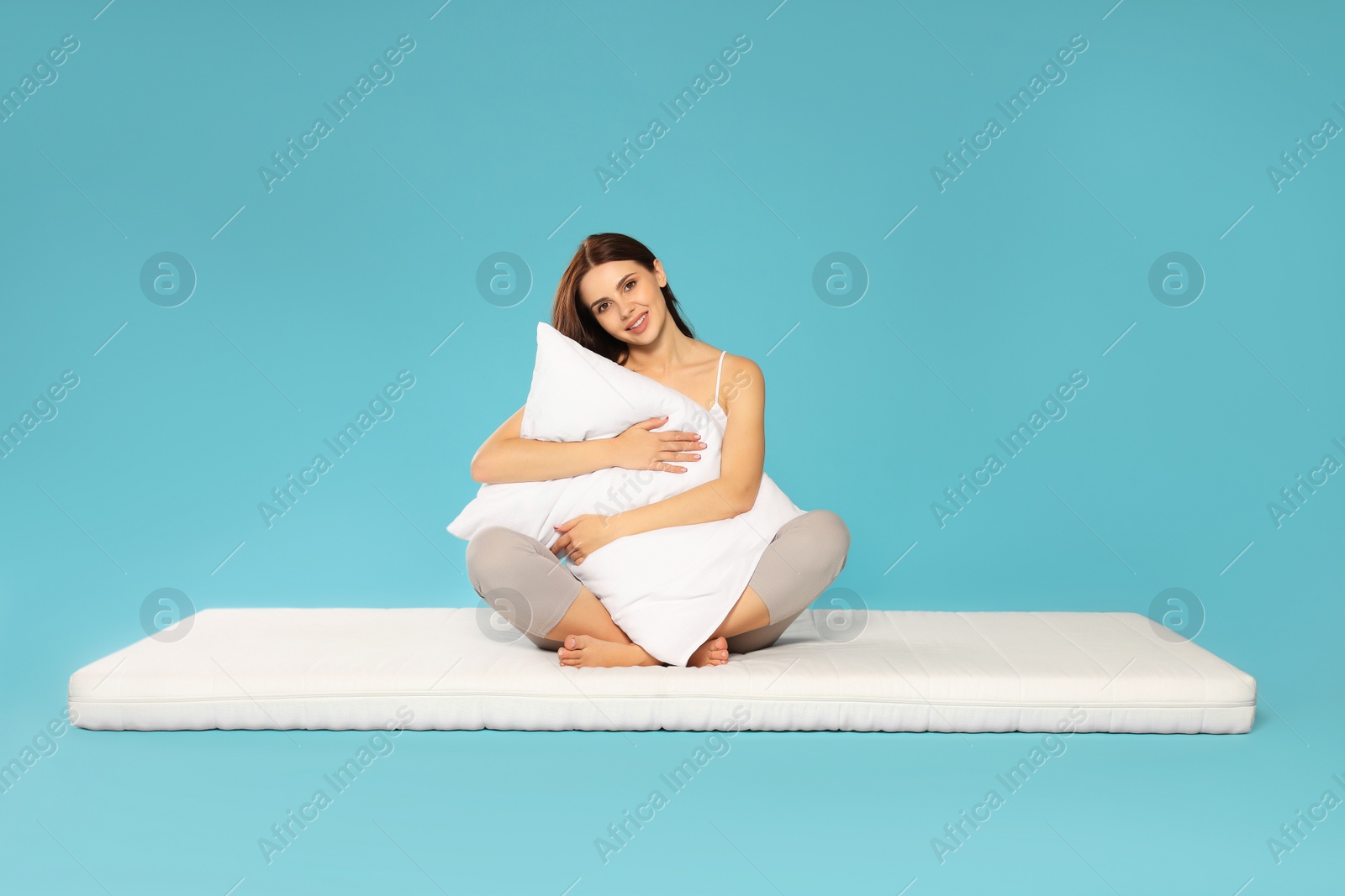 Photo of Young woman on soft mattress holding pillow against light blue background