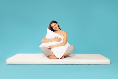 Young woman on soft mattress holding pillow against light blue background