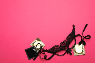 Photo of Lace mask and condoms on pink background, top view with space for text. Sex game
