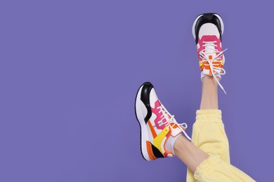 Photo of Woman wearing pair of new stylish sneakers on purple background, closeup. Space for text