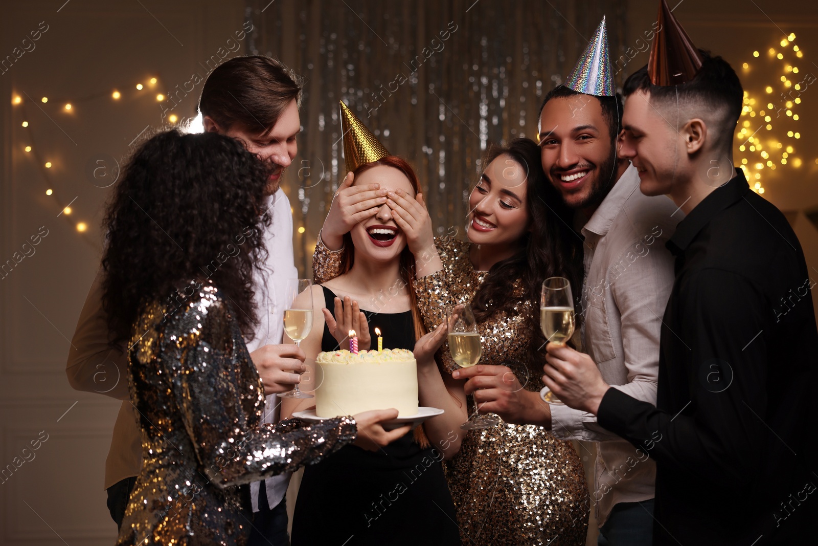 Photo of Happy friends with tasty cake and glasses of sparkling wine celebrating birthday indoors