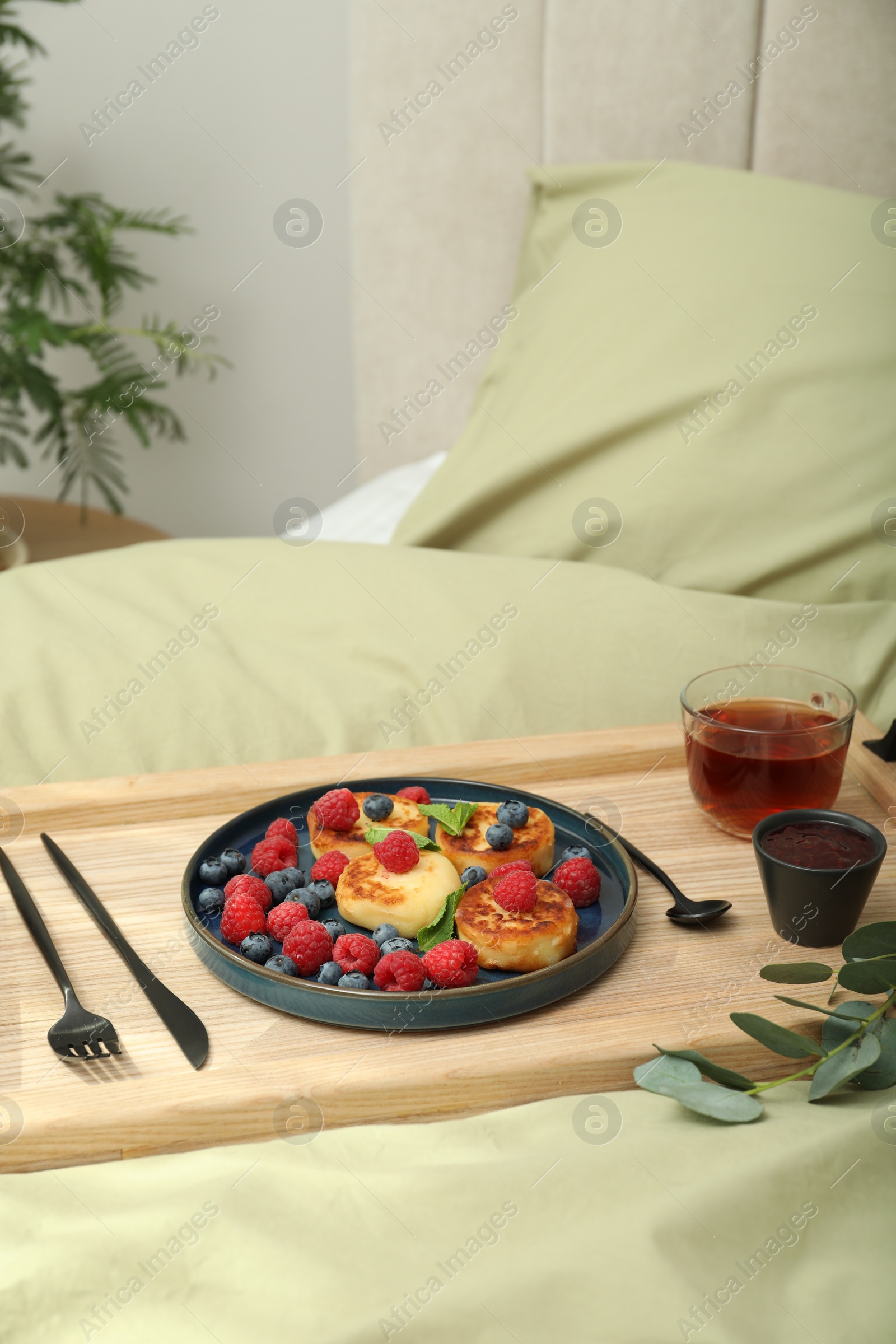 Photo of Tasty breakfast served in bedroom. Cottage cheese pancakes with fresh berries and mint on wooden tray