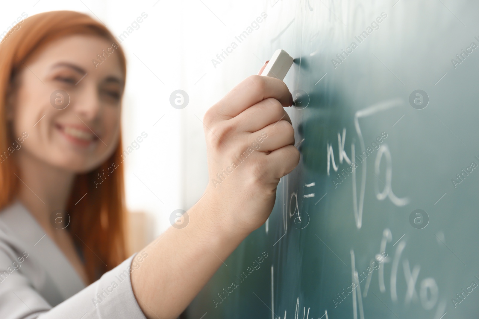 Photo of Beautiful young teacher writing on blackboard in classroom