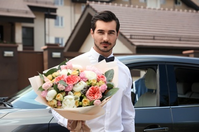 Young handsome man with beautiful flower bouquet near car outdoors