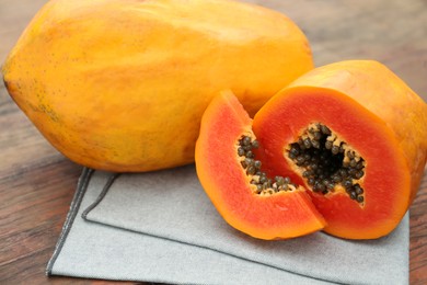 Photo of Ripe cut and whole papaya fruits on wooden table, closeup